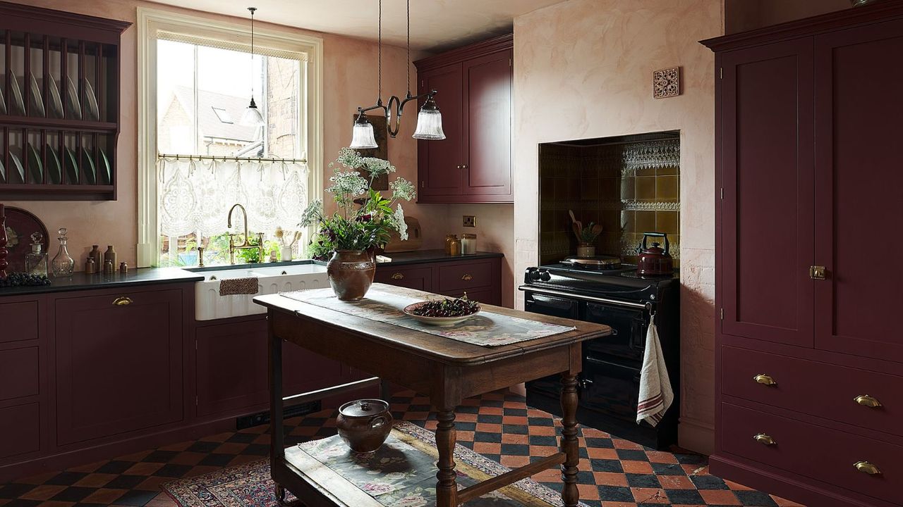 A small burgundy kitchen with small checkerboard floor tiles and a work table island