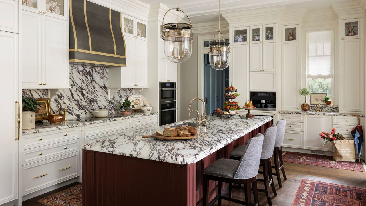 a white traditional kitchen with tall cabinetry, a statement marble countertop and splashback, a dark red island with marble and red vintage rugs