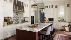 a white traditional kitchen with tall cabinetry, a statement marble countertop and splashback, a dark red island with marble and red vintage rugs