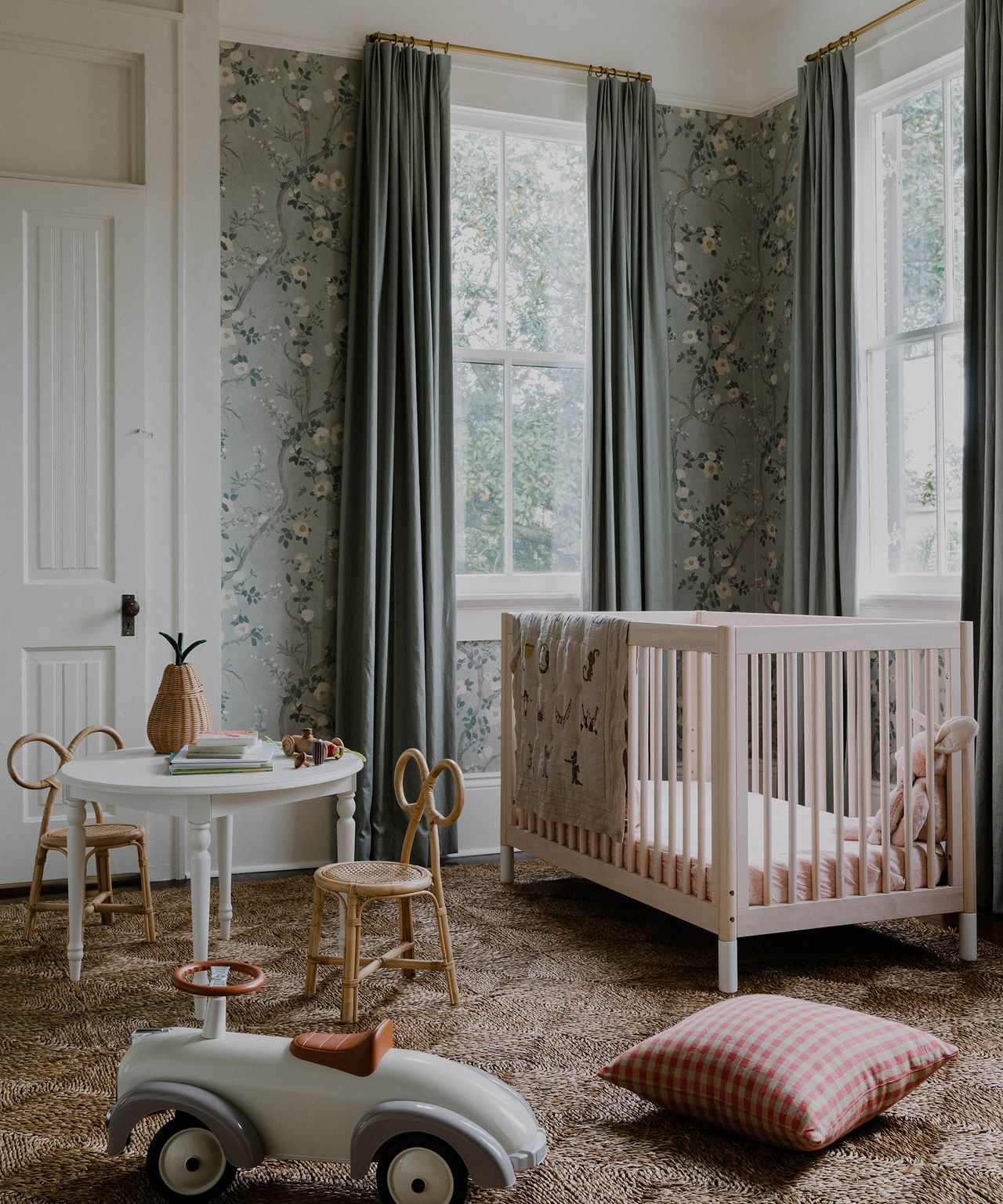 kid's bedroom with cot in one corner, toys on the floor and floral wallpaper on the walls