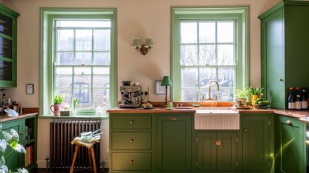 A small kitchen with green cabinets, copper countertops, warm neutral walls, and a fluted sink