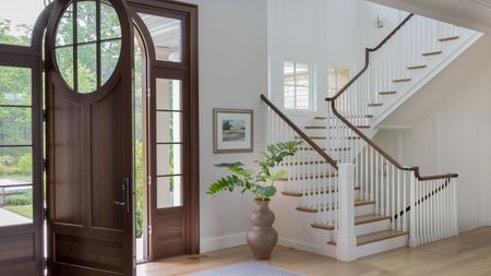 Large white, bright entryway with open wooden door and winding stair case showing step up to first floor, and down to basement level. It all features extensing hardwood flooring 
