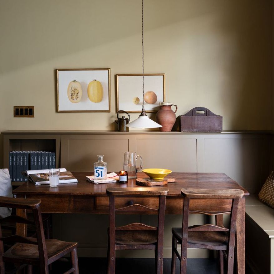 Light taupe dining corner with built in L-shaped benches in dark taupe paint, mid-century wooden table with four dining chairs, and built-in floor-to-ceiling cabinetry on the left