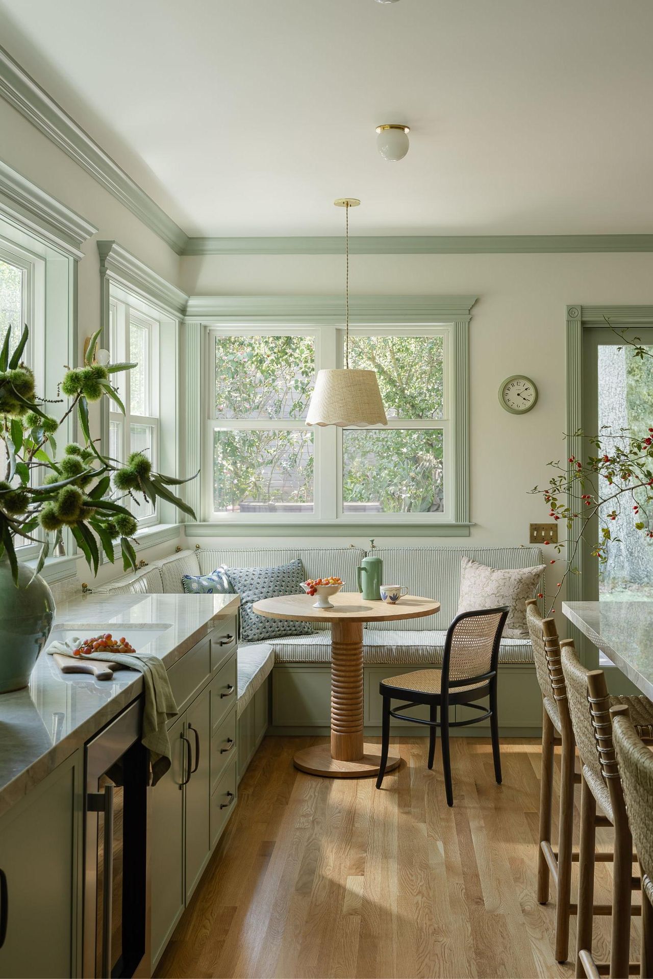 Split image: A light green kitchen featuring a breakfast nook with a round table and a built-in bench on the left, and a detailed view of a built-in pantry with open shelving and drawers on the right.