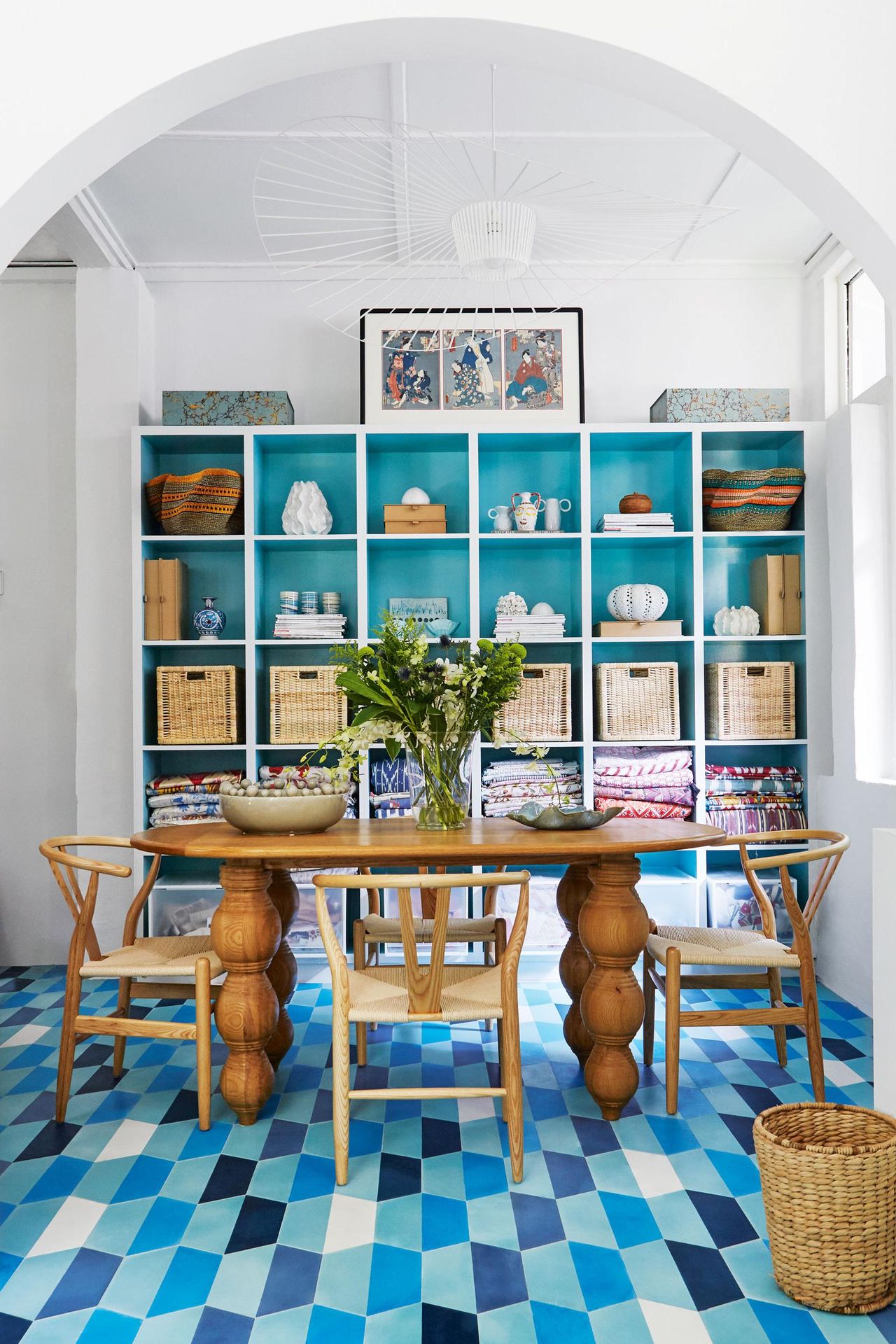 Dining table and chairs beside display shelves and archway in the foreground.