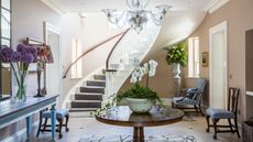 Entryway with pale pink walls, round wooden table with orchid, chandelier, mirror on wall and blue console table underneath