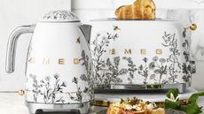 A SMEG kettle and toaster with grey flower and bee motifs on white bases, with stainless steel accents. 