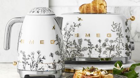 A SMEG kettle and toaster with grey flower and bee motifs on white bases, with stainless steel accents. 