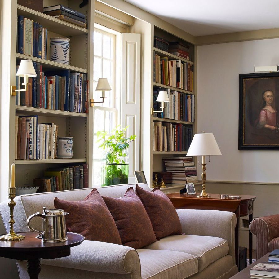 A cozy living room with build in book shelves between windows. A cream sofa in front beside a brown upholstered arm chair.