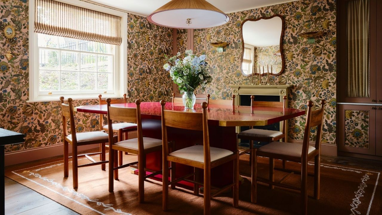 floral wallpapered dining room with a large red gloss lacquered table, wooden antique chairs with ball detailing, a large rug with border detail and a fireplace and mirror