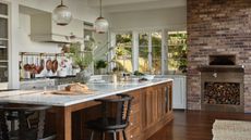 A spacious, sunlit kitchen featuring a large oak island with a marble countertop, black spindle stools, and vintage-style glass pendant lights